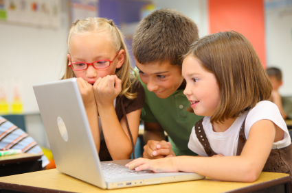 Three kids look at a laptop computer.

