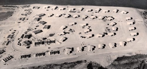 An aerial black and white photo showing houses under construction on a sandy island.