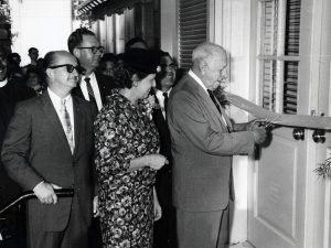 A man cuts a ribbon in front of a doorway while other people look on.