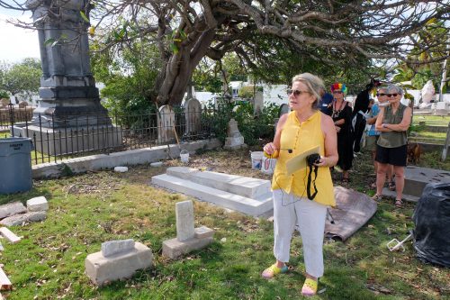 A woman stands in a graveyard with several people behind her.