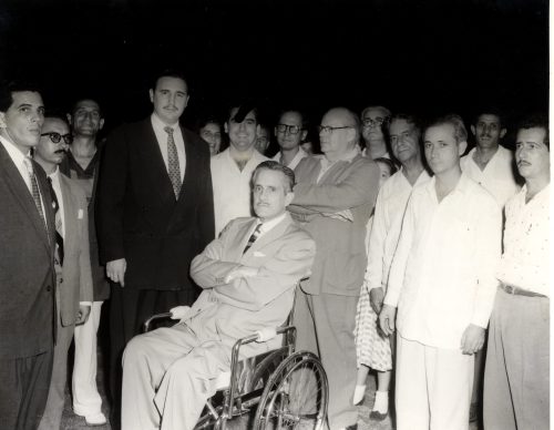 A group of men stand around behind one man sitting in a wheelchair.
