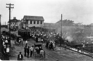 A group of people stand in a street while smoke rises from the ground nearby.