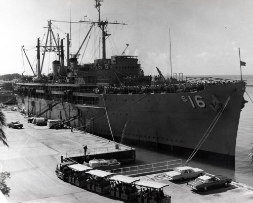 A large navy ship is tied up to a pier.