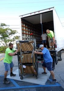Four people load a rack of bound volumes onto a truck.