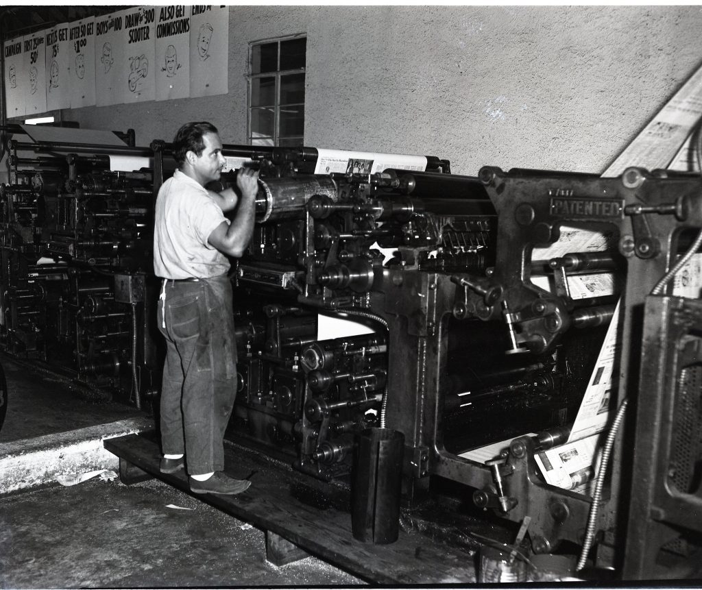 A man stands next to a printing press.