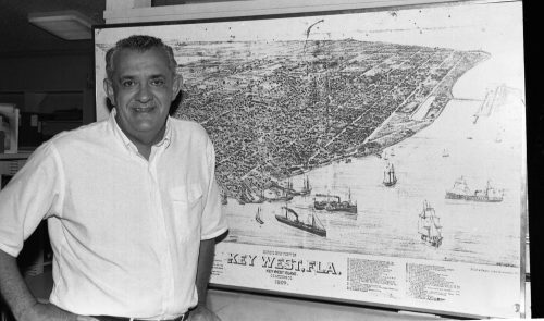 A man stands in front of an aerial image of an island labeled Key West, F L A.
