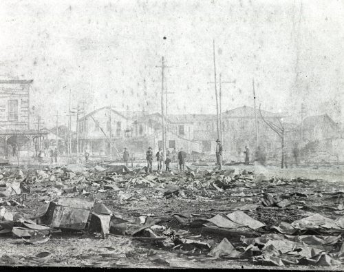 A group of figures standing near burned down buildings.