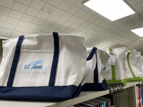 A row of canvas tote bags with a logo that says Monroe County Public Library