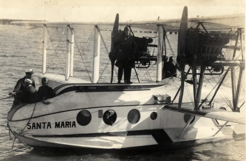 A seaplane in the water with several people on top of it and the name Santa Maria on the fuselage.