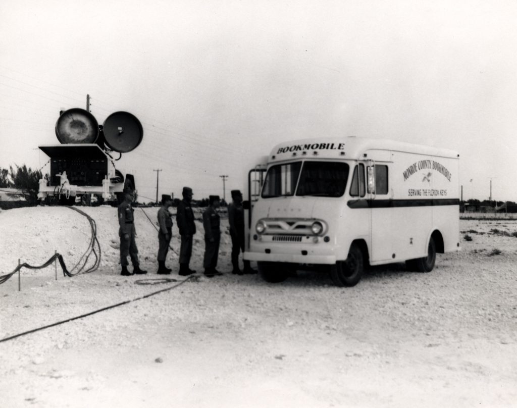 A row of people in uniform lined up next to a van labeled Monroe County Bookmobile serving the Florida Keys.