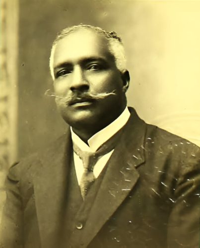 A photo of a man wearing a dark coat and tie and white shirt.