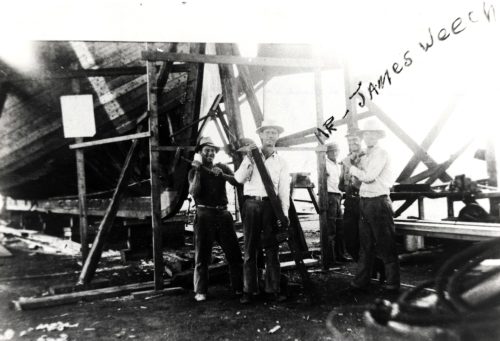 Five men stand under scaffolding with the hull of a ship. Handwritten on the photo is Mr. James Weech.