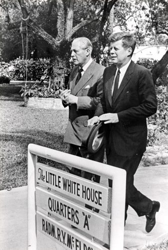 Two men walk past a sign that reads The Little White House Quarters A.