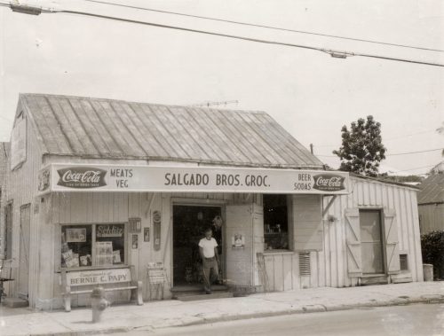A man stands in the doorway of a wooden building with a sign that says Salgado Brothers Grocery over the door.