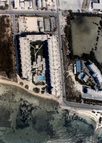 Aerial view of a shoreline with a three-sided building complex around a pool on land.