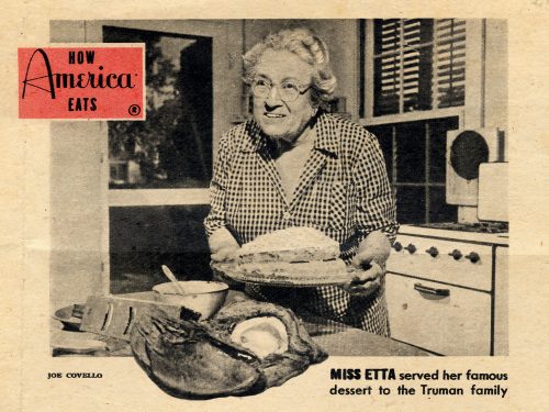 How America eats. Miss Etta served her famous dessert to the Truman Family. Photo of a woman holding a cake with an open coconut on the table in front of her.