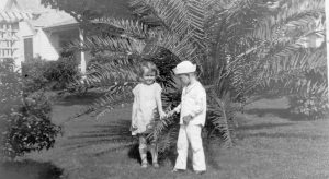 Two children, one wearing a sailor suit, in front of a palm.