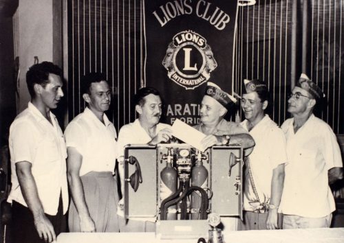 Six men stand in front of a banner that reads Lions Club.