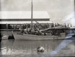 A boat moored to a dock with many people on the boat and on the dock.