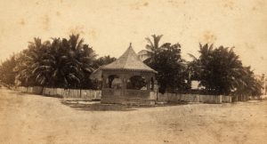 a bandstand in an open area in front of a picket fence.