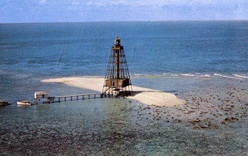 A small island with a screwpile lighthouse attached to a dock with a small shed at the end and a boat tied to it.