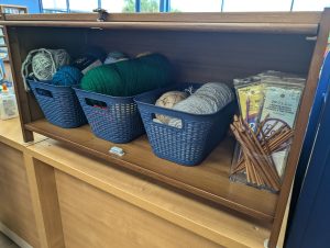 Three baskets of yarn and a bin of crochet and knitting needles on a shelf