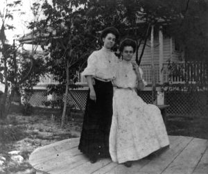 Two women with their arms around each other, one sitting, one standing.