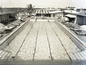 A large swimming pool with diving boards and lound chairs on either side.