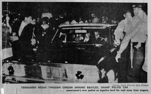 Photo of a police car with people around it. Caption reads Teenagers break through cordon around Beatles, swamp police car ... cameraman's arm jostled as deputies herd the mob away from singers. Citizen Staff Photos, Don Pinder.