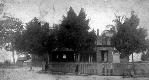 A building with a monument, a picket fence and trees with two children in front of it.