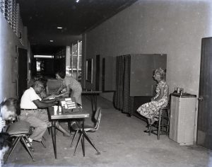 Several people in a hallway with a table and several booths with curtains.