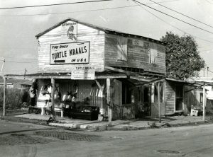 A two-story building in bad repair with signs on the side reading Half Shell Raw Bar and the only Turtle Kraals in USA.