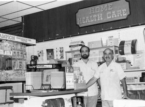 Two men stand in a store with a sign on the wall reading Home Health Care.