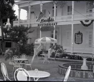 A patio area with tables in front of a two-story building with porches and signs that read Dedeks restaurant.